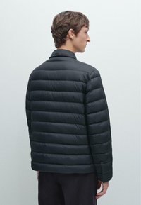 Schwarze Daunenjacke mit gesteppter Optik, ausgestattet mit Stehkragen und glatter Textur, von hinten vor einem hellen Hintergrund zu sehen.