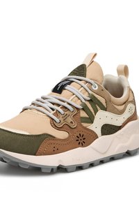 Beige and green sneaker featuring a mix of materials, textured accents, varied shapes, and white laces. Sturdy sole with gray tread.