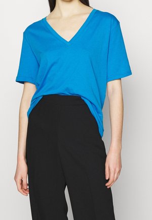 Turquoise katoenen T-shirt met een diepe V-hals, korte mouwen en een losse pasvorm, gecombineerd met zwarte hoge taillebroeken.