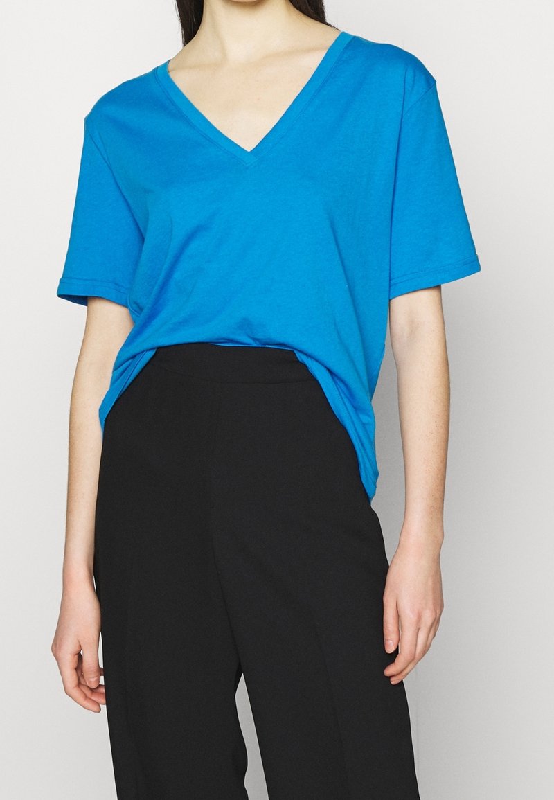 T-shirt en coton turquoise avec un col en V profond, des manches courtes et une coupe décontractée, associé à un pantalon noir taille haute.