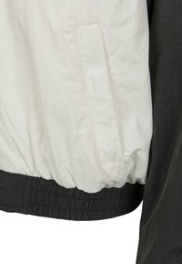 Chaleco cortavientos blanco y negro, con un acabado texturizado, dobladillo elástico y un bolsillo lateral en la sección blanca.