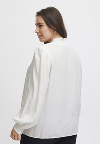 Weiße Bluse mit vertikalen Streifen, langen Puffärmeln und einer gerafften Ausschnitt. Strukturierter Stoff. Die Rückansicht zeigt ein glattes Design und eine schlichte Silhouette.