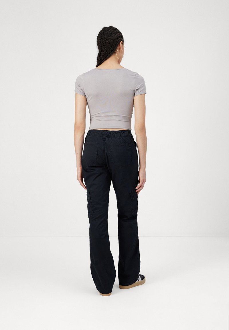 Graues, enges T-Shirt mit kurzen Ärmeln, kombiniert mit schwarzen Cargo-Hosen, die seitliche Taschen, einen elastischen Bund und ein gerades Bein haben.