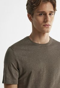 Olivegrünes T-Shirt aus weichem Stoff, mit Rundhalsausschnitt und kurzen Ärmeln, einer glatten Textur und minimalen Designdetails.