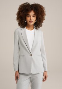 Světlě šedý blazer s jedním knoflíkovým zapínáním, klopami a předními kapsami. Vyznačuje se přiléhavým střihem a hladkou texturou látky.