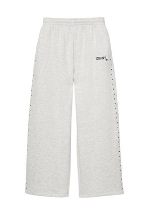 Pantalon de jogging gris clair à jambes larges avec ceinture élastique, petits clous noirs le long des côtés, et "SOHO NY" imprimé près de la poche gauche.
