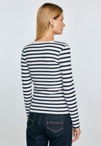 Gestreiftes Langarmshirt aus navy- und weißen gerippten Stoff. Verfügt über einen runden Halsausschnitt und eine schmale Passform, kombiniert mit dunklen Denimhosen.