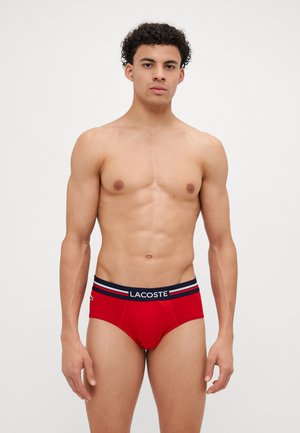 Röda kalsonger i boxermodell med en mörk midja med vita och marinblå ränder, prydda med Lacoste-logotypen på framsidan.