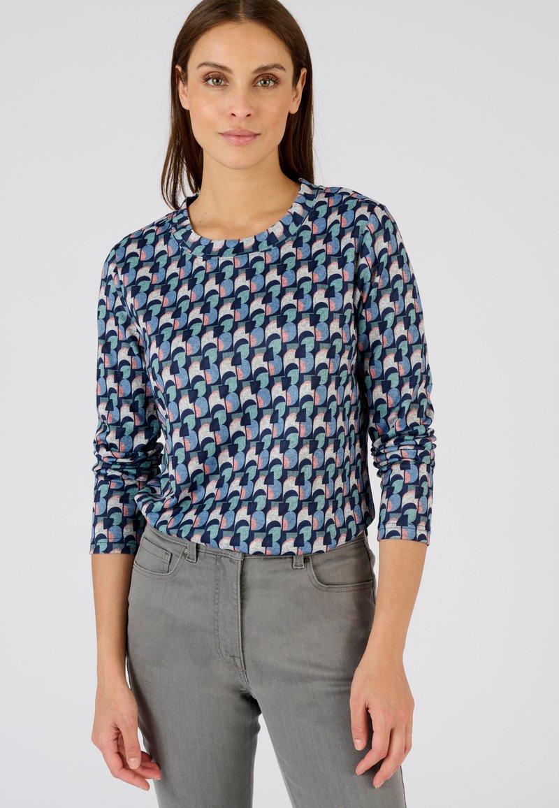 Patroon met lange mouwen in marineblauw met geometrische vormen in lichtblauw, roze en creme. Ronde hals, zachte stof, slim-fit stijl. Gestyled met grijze broek.