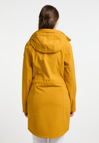 Cappotto giallo senape da donna con cappuccio, vita arricciata e tessuto morbido. Presenta maniche lunghe e un taglio di media lunghezza, con dettagli minimi.