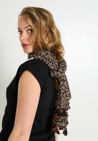 Bufanda de estampado de leopardo en tonos marrones y negros, con flecos en los extremos. Tejido ligero con una textura suave.