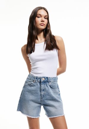 Shorts in denim bluastro con orli sfrangiati, vita alta e tasche frontali. Abbinati a un top aderente bianco.