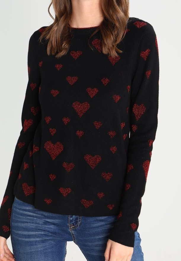Zwarte trui met rode glitterhartpatronen, ronde hals en lange mouwen. Gepaard met blauwe jeans, voegt de gestructureerde stof visuele interesse toe.