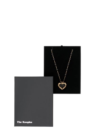 Collier en pendentif en forme de cœur en or avec des perles noires, présenté dans une boîte en velours noir. La boîte présente un logo discret en blanc sur le couvercle.