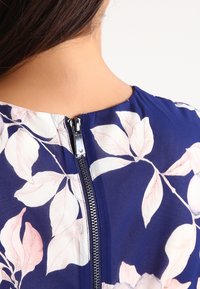 Marinblå klänning med blommönster, har en slät textur och en mittdragkedja i ryggen som framhäver den eleganta blommiga designen.