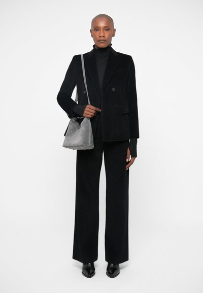 Sort kordfløjs dobbeltknappet blazer og matchende brede bukser. Grå ruskind skuldertaske, spidse sorte sko. Strømlinet, minimalistisk design.