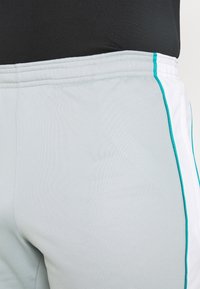 Ljusgrå sportshorts med en mjuk yta, med turkosa detaljer och en kontrasterande vit sidopanel samt en elastisk midjeband.