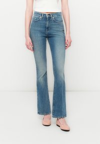 Jeans in denim blu chiaro a zampa d'elefante con vita alta, leggera scoloritura e design classico a cinque tasche, abbinati a ballerine rosa.