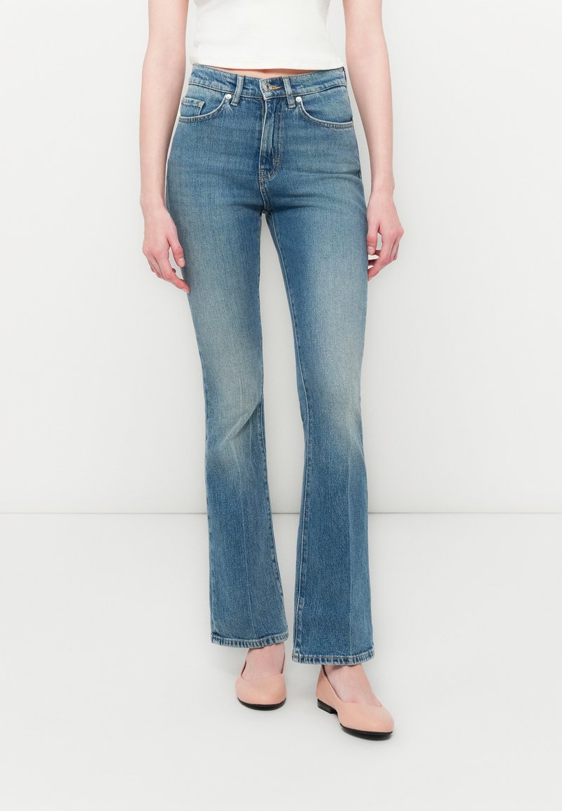 Jeans in denim blu chiaro a zampa d'elefante con vita alta, leggera scoloritura e design classico a cinque tasche, abbinati a ballerine rosa.