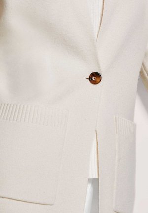 Beige cardigan van zacht stof, voorzien van een bruine knoopsluiting, geribbelde zakken en een zijsplit voor een relaxte pasvorm.