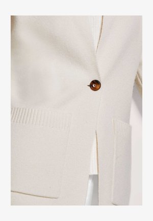 Beige cardigan van zacht stof, voorzien van een bruine knoopsluiting, geribbelde zakken en een zijsplit voor een relaxte pasvorm.