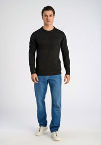 Czarny sweter wykonany na drutach z teksturowymi paskami, dopasowany do niebieskich dżinsów i białych trampków. Sweter ma prążkowane mankiety i dół.