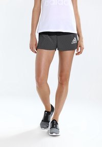 Svart- och vitrandiga träningsshorts med elastisk midja och "Adidas"-logotyp. Matchas med grå sneakers med blixtlåsstängning.