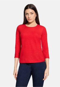 Czerwona, teksturowana bluzka z długim rękawem, okrągłym dekoltem i dopasowanym krojem, zestawiona z ciemnymi dżinsami. Casualowy i prosty fason.