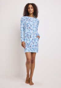 Abito a maniche lunghe in azzurro chiaro con motivi floreali in tonalità di blu scuro. Presenta una scollatura rotonda e tasche laterali. Tessuto morbido.