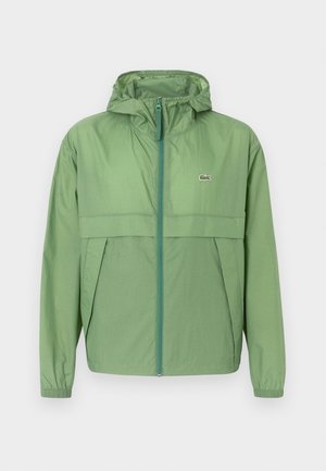 Lichtgroene hooded jack met een ritssluiting aan de voorkant, voorzien van een borstpaneel en elastische manchetten. Lacoste-logo op de linkerkant van de borst. Soepele textuur.