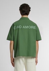 Maglietta verde a maniche corte in cotone, con grande scritta "CIAO AMORE" sul retro. Vestibilità comoda e orlo dritto.