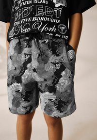 Zwarte shorts met een wit golvend lijnenpatroon, elastische tailleband met trekkoord en zijzakken voor functionaliteit.