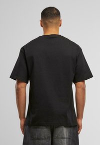 Camiseta de algodón negra de manga corta, con cuello redondo clásico y corte relajado, mostrada desde la parte posterior con una textura suave.