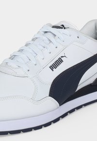 Бяла маратонка Puma с черна ивица отстрани, бели връзки и лого на Puma над ивицата, показваща страничните и предни детайли на обувката.