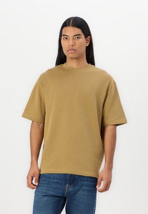 T-shirt à manches courtes et col rond en tissu coton kaki. Présente une coupe décontractée et un ourlet droit. Porté avec un jean en denim bleu.