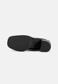 Suela de zapato negra hecha de goma, con un agarre texturizado que presenta estrías horizontales y verticales. Forma redondeada con una ligera elevación del tacón.