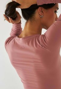 Dopasowana bluzka z długim rękawem wykonana z materiału w kolorze przygaszonego różu. Gładka faktura, okrągły dekolt oraz detal w postaci logo serca z tyłu przy karku.