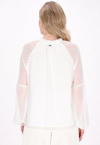 Weiße Bluse mit durchsichtigen Puffärmel im Polka-Dot-Design, gerafftem Ausschnitt und elastischen Bündchen. Glatte Oberfläche mit lässiger Passform und Rückenpasse.