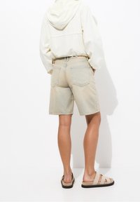 Lysfarvede denimshorts med en afslappet pasform, der har baglommer og synlige sømme. Sættet er komplet med en creamfarvet hættetrøje og beige sandaler.