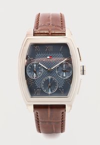 Ρολόι χειρός Tommy Hilfiger με ορθογώνια ασημένια κάσα, καφέ λουράκι από δέρμα, μπλε υφασμένο καντράν, ρωμαϊκούς αριθμούς και τρεις υποκαντράν για ημέρα, ημερομηνία και 24ωρη ένδειξη.