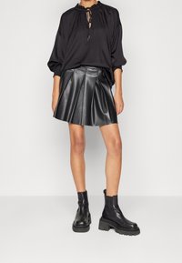 Czarna bluzka z marszczonym dekoltem i sznurkiem, w zestawieniu z czarną plisowaną skórzaną spódnicą i masywnymi czarnymi botkami za kostkę.