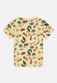 Camiseta amarilla de manga corta con un estampado tropical que incluye palmeras, gafas de sol y gráficos de marca en naranja y verde.