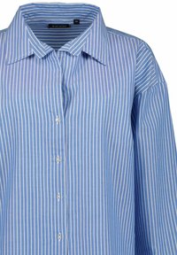 Camicia azzurro chiaro con righe verticali bianche, dotata di colletto classico e sei bottoni frontali. Realizzata in tessuto di cotone tessuto.