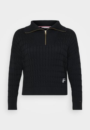 Svart strikket genser med glidelås krage, teksturert kabelmønster, ribbede mansjetter og en liten brodert logo på kanten.