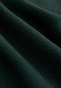 Dunkelgrüner gestrickter Stoff mit einer glatten Textur, die ausgeprägte horizontale Rippmuster und subtile Farbnuancen aufweist.