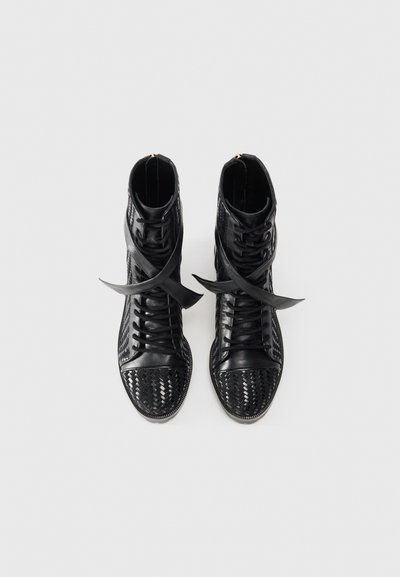 Svarta läderstövletter med vävd textur på ovansidan, rund tå och platta skosnören. Dekorativa korsband är i centrum.