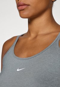 Grå atletisk singlet med rund halsutskjæring og tynne stropper, med en hvit Nike-swoosh-logo på brystet. Glatt tekstur.