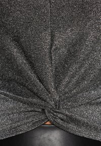 Svart texturerad tyg med metallisk lyster, med en knuten detalj i mitten som hänger smidigt runt en mörk läderyta.