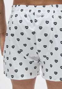 Boxer bianchi con un motivo ripetuto di piccoli cuori neri con il testo "Carhartt WIP", fascia elastica in vita e design a vestibilità rilassata.