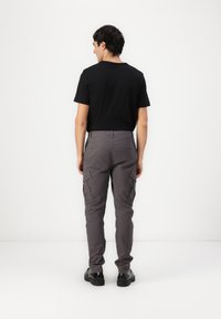 Pantalones cargo grises con bolsillos laterales, un ajuste entallado y una resistente mezcla de algodón, combinados con una camiseta negra y zapatos negros.